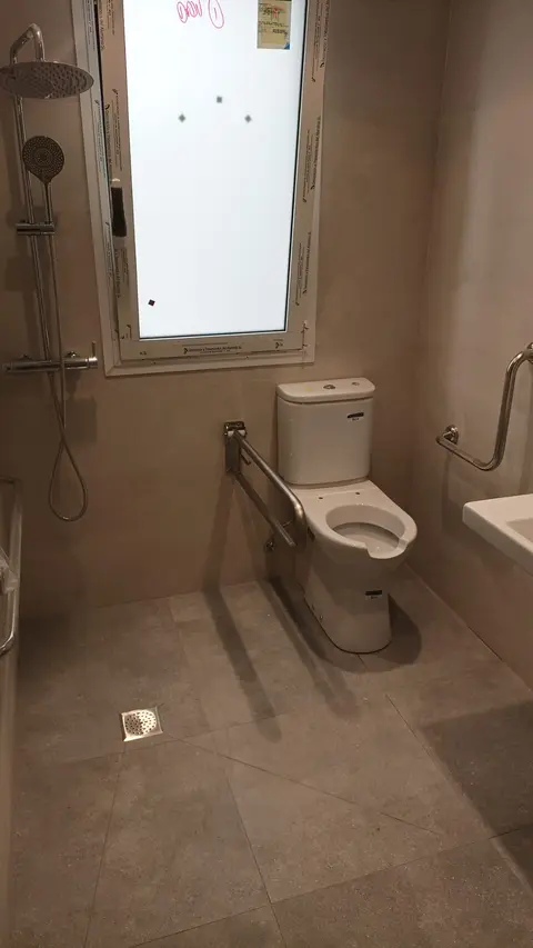 Baño adaptado con ducha a ras de suelo, barras de apoyo abatibles e inodoro con apoyo