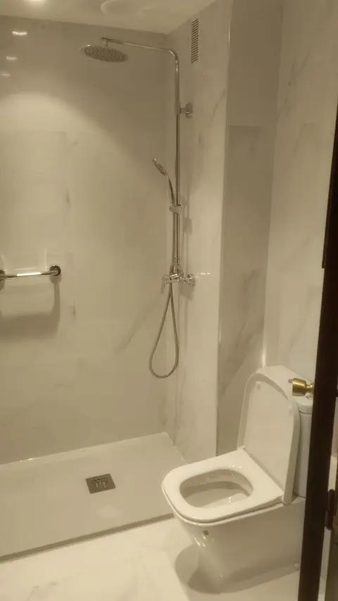 Baño completo con ducha de lluvia, revestimiento de efecto mármol y plato blanco