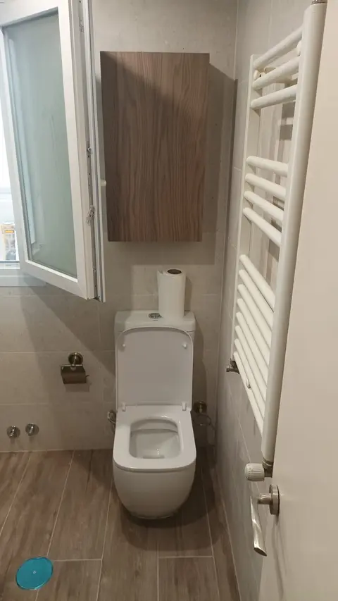 Baño reformado con suelo de imitación madera, toallero blanco y armario alto