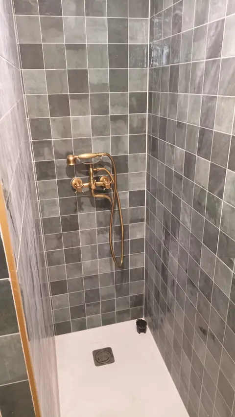 Ducha con azulejo verde artesanal, plato blanco y grifería dorada de estilo clásico