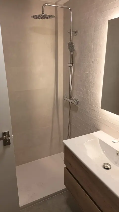 Ducha de lluvia con plato blanco y mueble de lavabo de madera en un baño reformado en Madrid