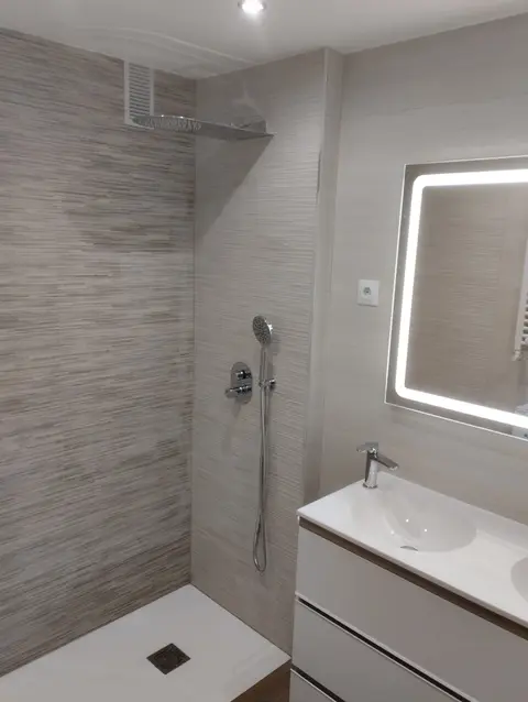 Ducha con plato blanco junto a lavabo con mueble blanco y espejo con luz LED