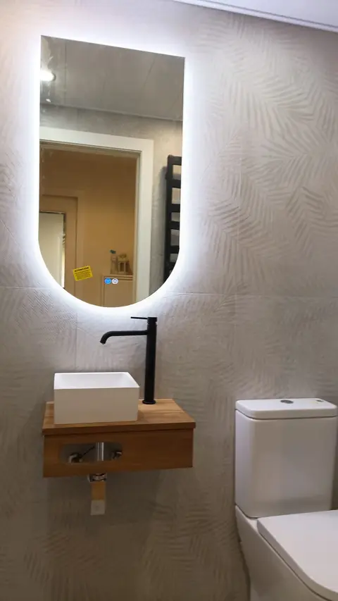 Lavabo sobre encimera de madera con grifería negra y espejo ovalado con luz LED