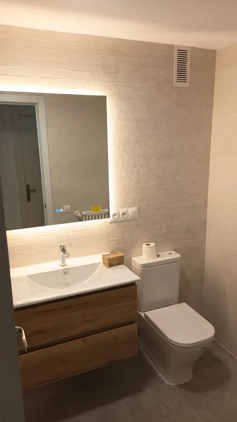 Mueble de lavabo de roble con espejo con luz LED indirecta en un baño reformado