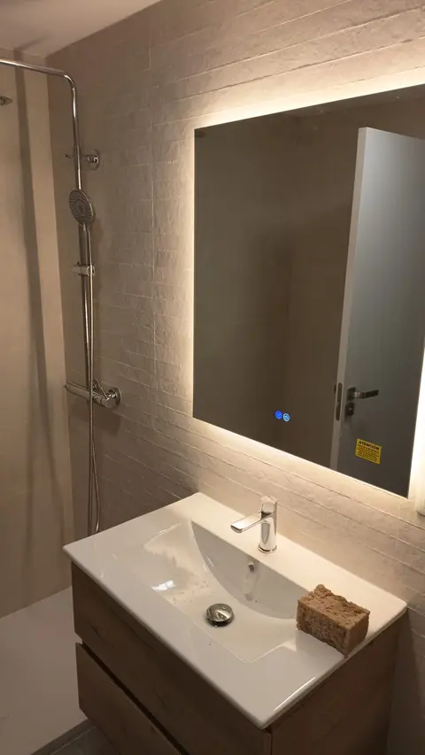 Lavabo con mueble de roble, espejo con luz LED y ducha de lluvia al fondo