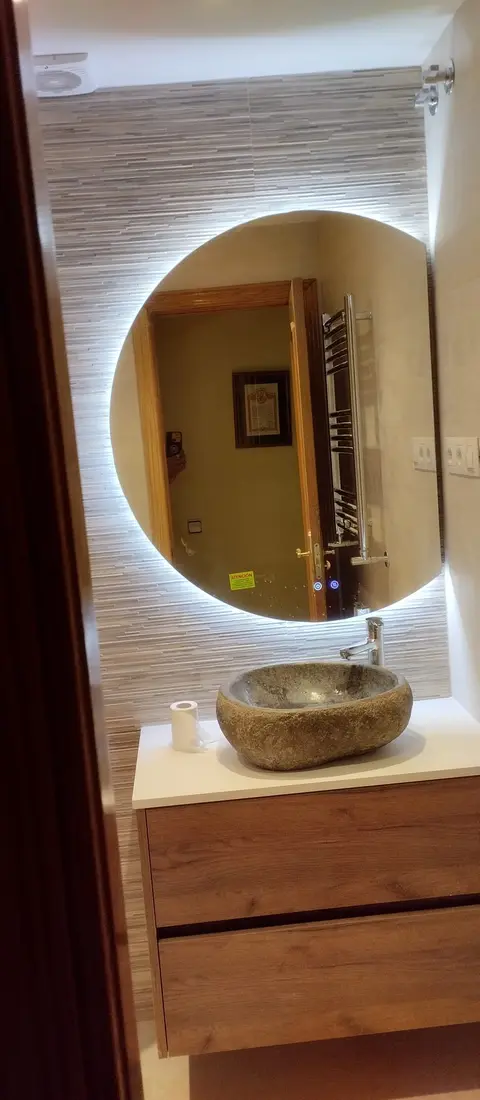 Lavabo de piedra natural sobre mueble de roble con espejo redondo con luz LED