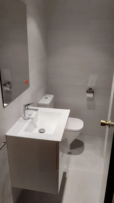 Lavabo suspendido blanco con mueble en un baño reformado en tonos grises