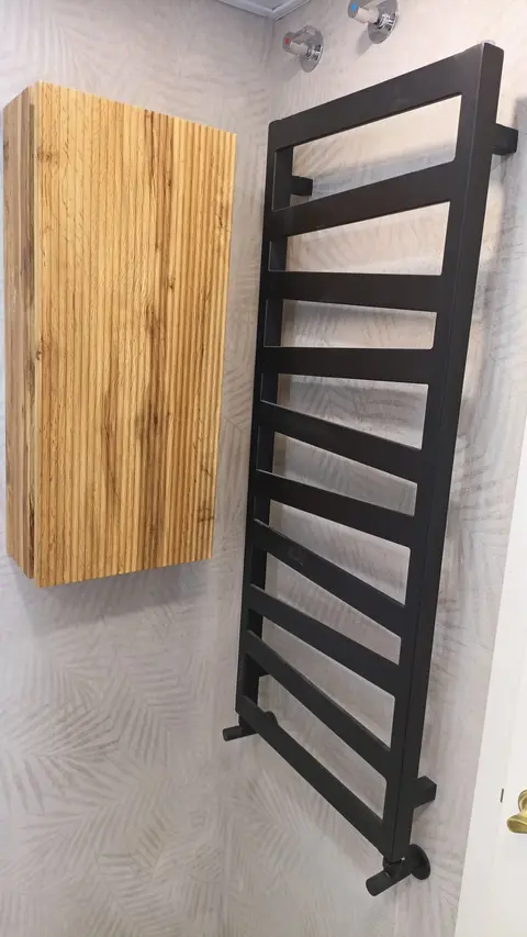 Toallero radiador negro y mueble alto de madera sobre revestimiento con relieve de hojas